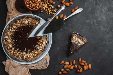 Çikolatalı pasta, çikolatalı pasta, fındıklı tatlı. Kesik bir parça. Kızarmış fıstık, badem ve fındık. Karanlık arka planda. Yukarıdan manzara. Yandan manzara. Metin için boşluk.