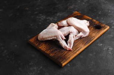 Koyu arkaplanda tahta kesim tahtasında pişirmek için baharatlı çiğ tavuk kanadı. Yukarıdan manzara. Yan görüş. Metin için boşluk.