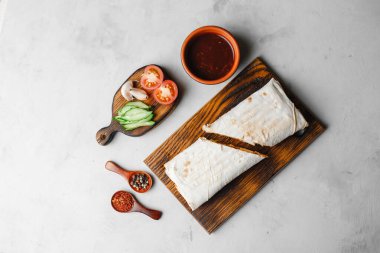 Ev yapımı Shawarma, burrito, sebzeli tavuk dürümü ve sos. İçindekilerin temiz bir alana sahip üst görünümü.
