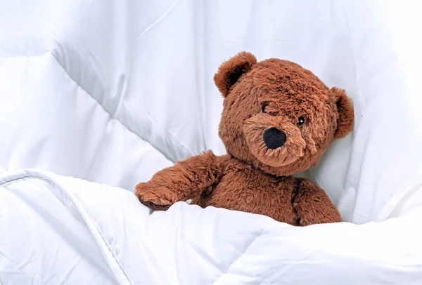 Teddy Bear in the crib under a white blanket. — Stock Photo, Image