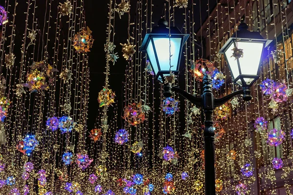 Renkli Noel çelenklerinin arka planında sokak lambası. Gece şehrinde Yeni Yıl süsleri.