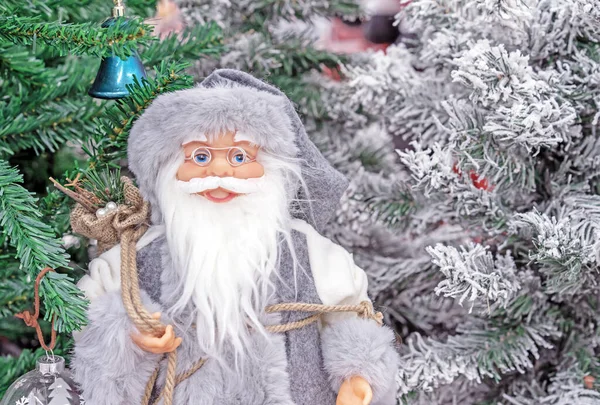 Giocattolo Babbo Natale in un cappotto grigio sullo sfondo degli alberi di Natale . — Foto Stock