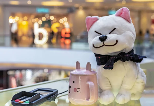 Soft toy of a cat and a pink mug next to the payment terminal in the store.