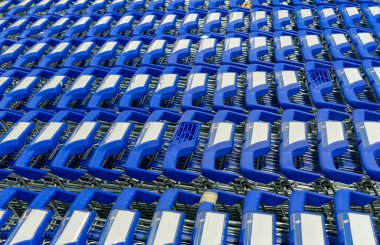 Süpermarketin girişine park edilmiş alışveriş arabaları. Koyu mavi saplı metal arabalar..