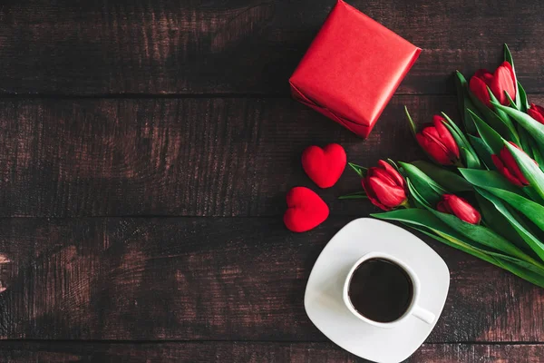 Buchet de lalele roșii pe un fundal din lemn cu o ceașcă de cafea. Flori de primăvară. Fundalul zilei mamei . — Fotografie, imagine de stoc