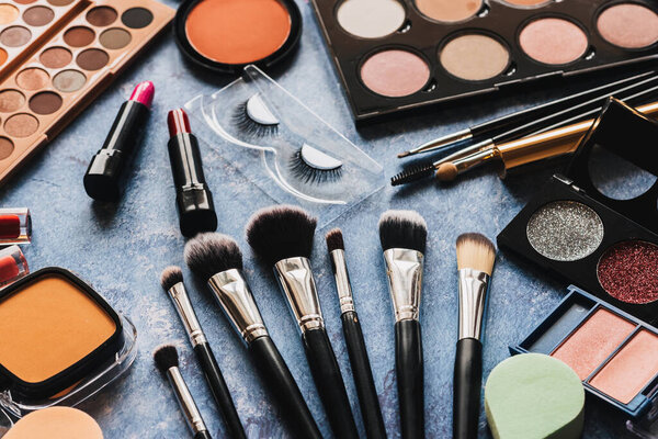 Various makeup products, brushes on blue background