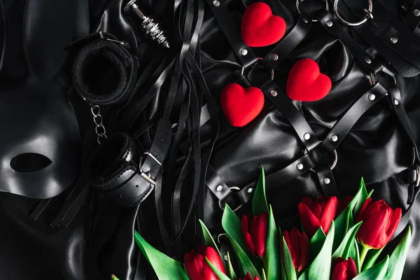 El día de San Valentín, un conjunto de juguetes para adultos sobre un fondo de seda negro. Tulipán rojo — Foto de Stock