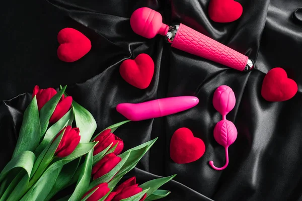 Verschiedene Sexspielzeuge auf schwarzem Hintergrund. Werbung für einen Sexshop. die Aussicht von oben. Frühling. Tulpen — Stockfoto
