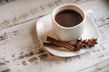 Hafif ahşap zemin üzerinde tarçın çubukları olan bir fincan kahve..
