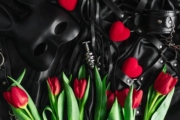 Explore the world of kinky play. Top view of bdsm leather kit against of a black silk. tulips — Stockfoto