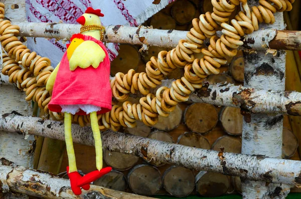 Festividades da maré negra. Decoração de lugares de comércio. Brinquedo-galo e bbundle de bagels, pendurado na cerca de bétula — Fotografia de Stock