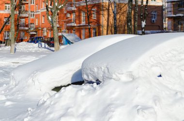Parked cars under snowdrifts in city yard after snowfall in March clipart