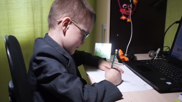 一个穿夹克的男孩做作业 他用铅笔把它写在一张纸上 偏远地区的生活 — 图库视频影像