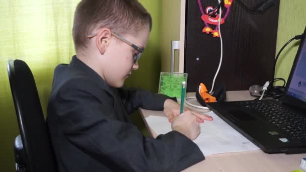上着を着た少年が宿題をする 彼は紙に鉛筆で書いています 遠隔地での生活 — ストック動画