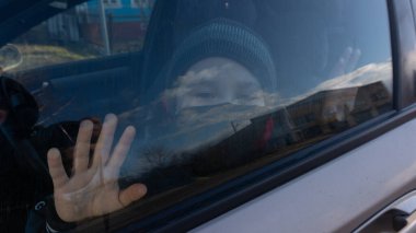 Siyah maskeli bir çocuk araba penceresinin arkasında.