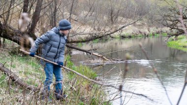 Dere kenarında sopalı bir çocuk. Gri şapkalı ve ceketli.