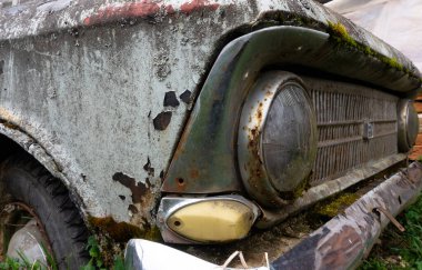 Terk edilmiş eski araba yosunla kaplanmış. Yerdeki tekerlekler büyümüş. Araba mezarlığı. Moskovalı.