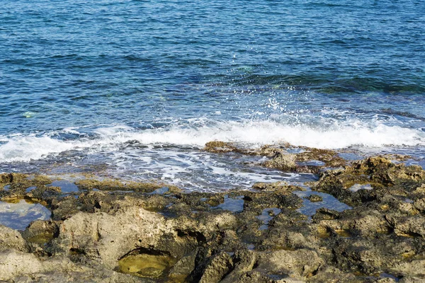 Le onde si infrangono su una spiaggia rocciosa, formando uno spray. Onde e spruzzi sulla spiaggia. Onde che si infrangono sulle rocce . — Foto Stock