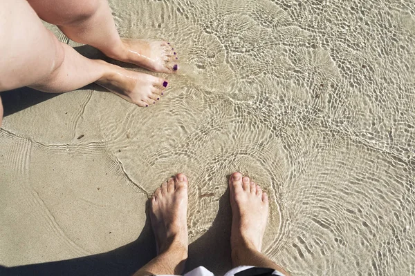 Deux paires sur le sable avec de l'eau de mer . — Photo