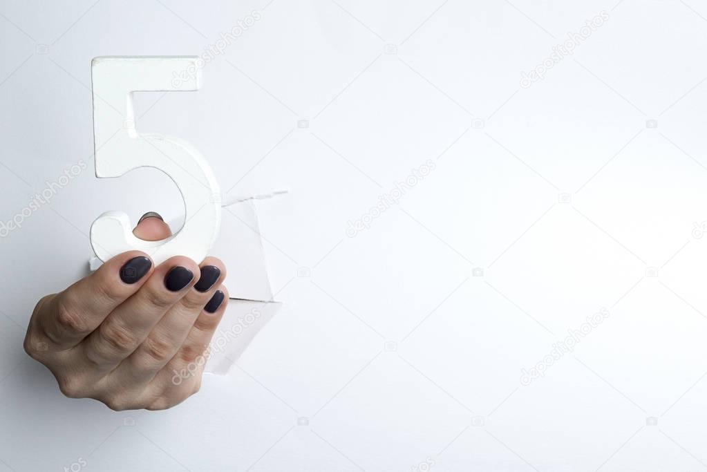 Female hand holding up the number 5 against a white
