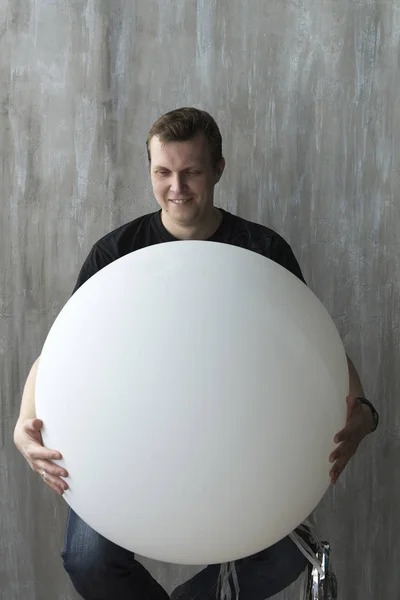 Un hombre sosteniendo una bola inflable sobre un fondo gris . —  Fotos de Stock