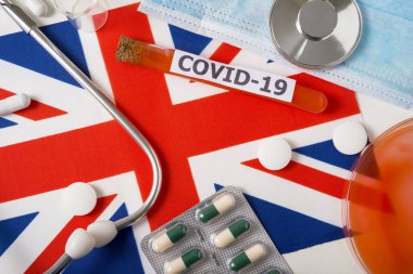 Coronavirus, Covid-19 konsepti. Üst düzey koruyucu solunum maskesi, steteskop, şırınga, İngiltere bayrağında haplar. Yeni bir Çin Coronavirüsü salgını.