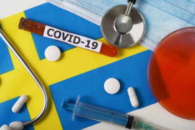 Coronavirus, Covid-19 konsepti. Üst düzey koruyucu maske, steteskop, şırınga, İsveç bayrağında haplar. Yeni bir Çin Coronavirüsü salgını.