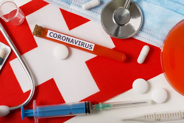 Coronavirus, nCoV concept. Top view protective breathing mask, stethoscope, syringe, pills on the flag of Switzerland. A new outbreak of the Chinese coronavirus