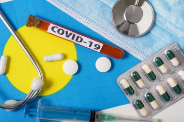 Coronavirus, COVid-19 konsepti. Palau bayrağındaki koruyucu bir maske, steteskop, şırınga ve haplar yukarıdan görülebiliyor. Yeni bir Çin Coronavirüsü salgını.