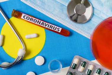 Coronavirus, NCoV konsepti. Palau bayrağındaki koruyucu bir maske, steteskop, şırınga ve haplar yukarıdan görülebiliyor. Yeni bir Çin Coronavirüsü salgını.