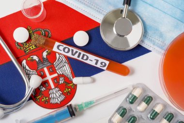 Coronavirus, COVid-19 konsepti. Sırbistan bayrağında üst düzey koruyucu solunum maskesi, steteskop, şırınga, tabletler var. Yeni bir Çin Coronavirüsü salgını.
