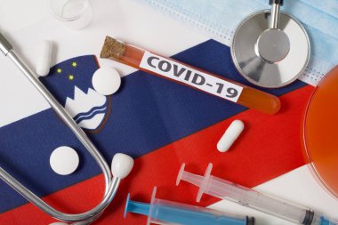 Coronavirus, COVid-19 konsepti. Üst düzey koruyucu solunum maskesi, steteskop, şırınga, Slovenya bayrağında tabletler. Yeni bir Çin Coronavirüsü salgını.