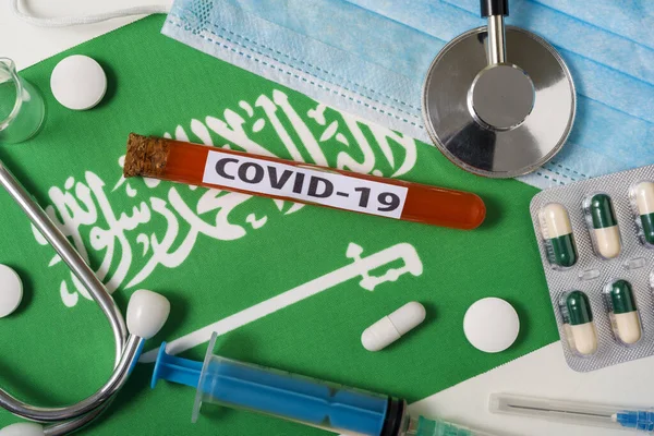 Coronavirus 概念Covid 俯瞰保护呼吸面罩 听诊器 注射器 挂在沙特阿拉伯国旗上的药片 中国头孢病毒的新爆发 — 图库照片