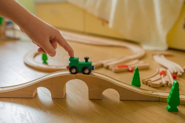 Çocuk, demiryolu ve yeşil bir lokomotifle ahşap bir demiryolu kullanıyor.