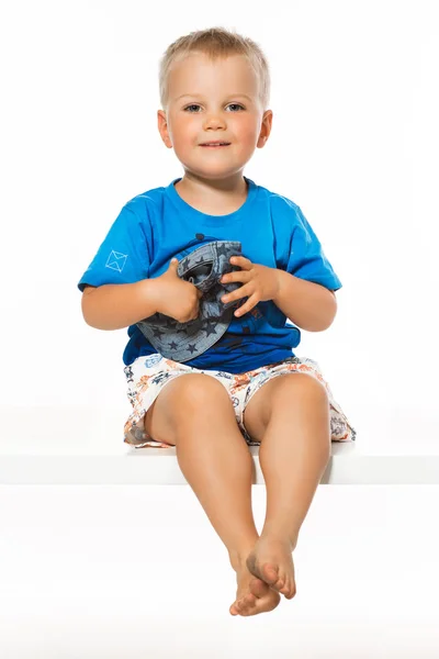 Niedlicher blonder Junge sitzt auf dem Tisch, weißer Hintergrund — Stockfoto