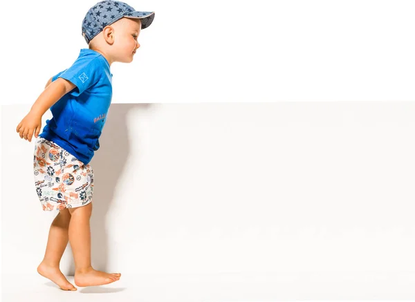 Niedlich lächelnder kleiner Junge schaut auf das leere weiße Plakat — Stockfoto