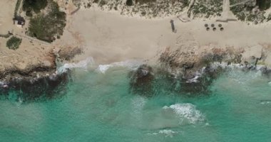 Turkuaz kristal deniz dalgaları üzerindeki bir dron tarafından kumsalda ve kayalarda kırılarak vuruldu.