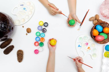 Paskalya sembolünün ortak geleneksel renklendirmesi. Eller, fırçalar, boyalar, paletler, beyaz arkaplanda yumurtalar.