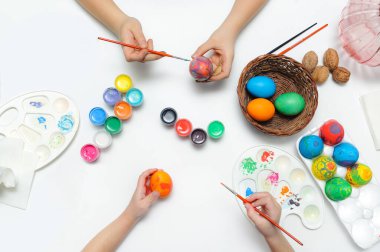 Paskalya için hazırlanıyorum. Çocuklar yumurtanın üstüne resim yapar. Yukarıdan beyaz arkaplanda görüntüle.