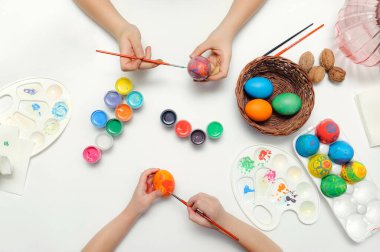 Paskalya sembolünün ortak geleneksel renklendirmesi. Eller, fırçalar, boyalar, paletler, beyaz arkaplanda yumurtalar.