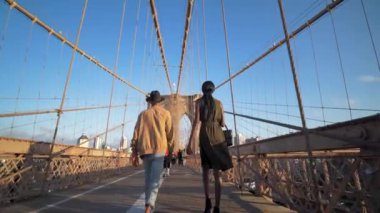 Genç siyah çift Brooklyn Köprüsü 'nde yürüyor. Lens günbatımını aydınlatıyor.