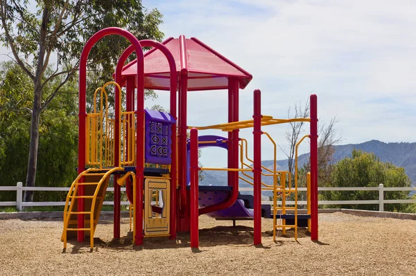 Small playground sits up on a hill with a fence and mountain range in the background.