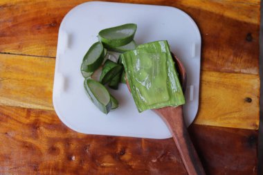 Aloe vera taze yapraklar dilimler ve jel ile ahşap bir kaşık üzerinde izole beyaz bir arka plan, 