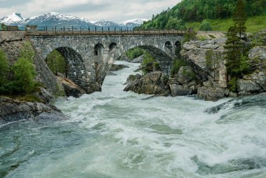 Bridge Over Rough Water:  A bridge made of heavy stone blocks stands above a whitewater river in the mountains of southwest Norway.