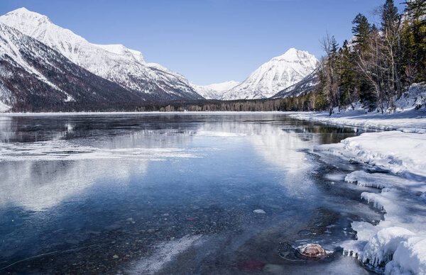 Montana Lake in Winter:  Snow covered mountains reflect from the icy surface of Lake McDonald in Glacier National Park.