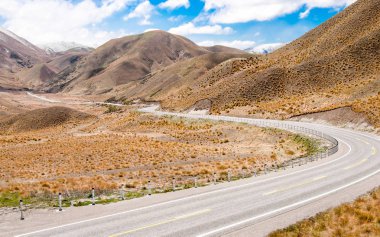 New Zealand Desert Mountain Pass:  A two lane highway curves through arid terrain toward Lindis Pass on New Zealands South Island.