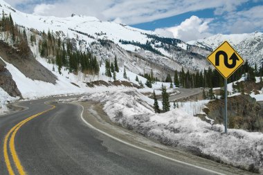 Switchback Road and Sign:  A sign warns of repeated sharp turns ahead on a mountain road in southwest Colorado.