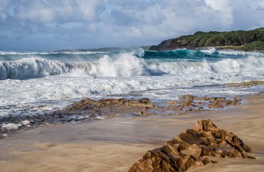Volcanic Beach:  Strong winds and an incoming tide create large waves that crash against a volcanic shelf at the edge of a beach in the Hawaiian Islands.
