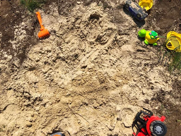 Sarı kamyon, kırmızı traktör ve kumdaki diğer oyuncaklar. Çocuklar açık hava oyuncakları