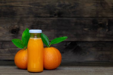 Cam şişelerde portakal suyu ve ahşap arka planda iki portakal..